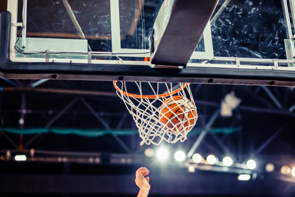 A basketball is seen going through a hoop with a player's hand extended upward underneath the net, showcasing the skill nurtured by a professional athlete's foundation.