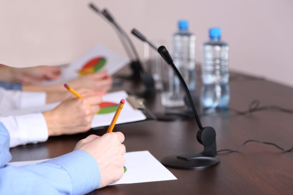 People's hands are shown writing on paper, with pie charts visible, at a conference table discussing complaints against a nonprofit.