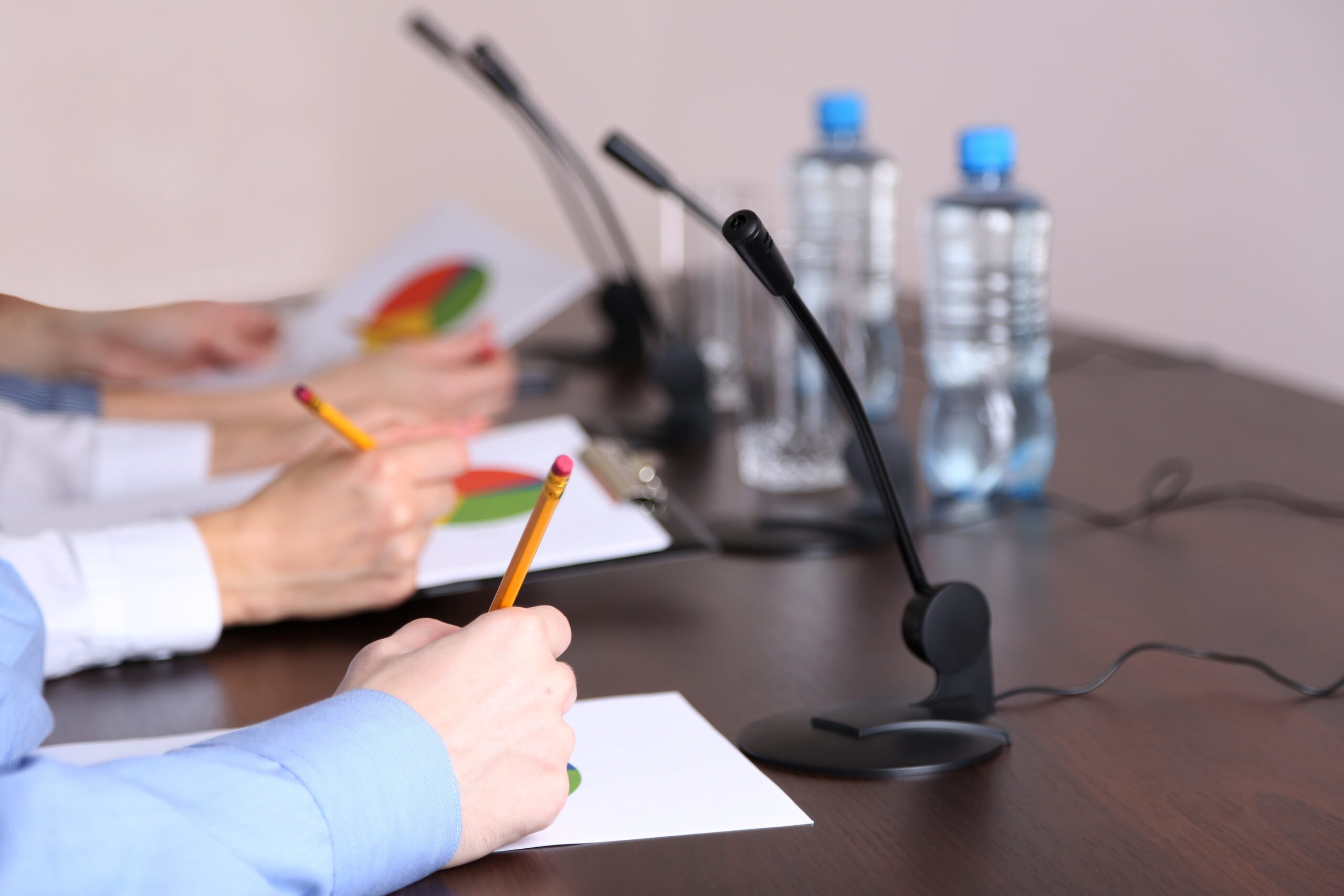 People's hands are shown writing on paper, with pie charts visible, at a conference table discussing complaints against a nonprofit.
