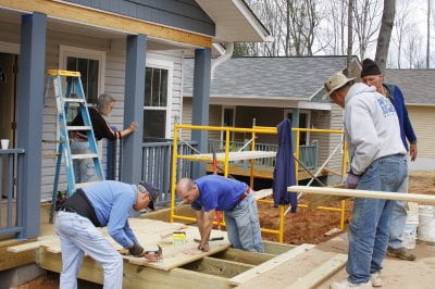 A group of people work on a wooden ramp outside a house, embodying the community-driven spirit often seen in the duties of nonprofit board of directors.